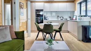 A compact living space with a dining area, kitchenette, and a green sofa. - Green Mews 3 By My Getaways (Hove)