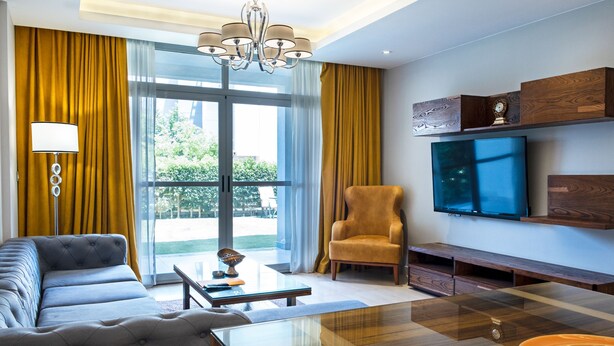 A modern living room with a sofa, armchair, coffee table, and a TV mounted on the wall. - Vesta - Luxury Apt- 2BR - CFC II (New Cairo)