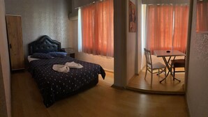 Un dormitorio con cama, un armario de madera, una mesita con silla y una ventana con cortinas naranjas.