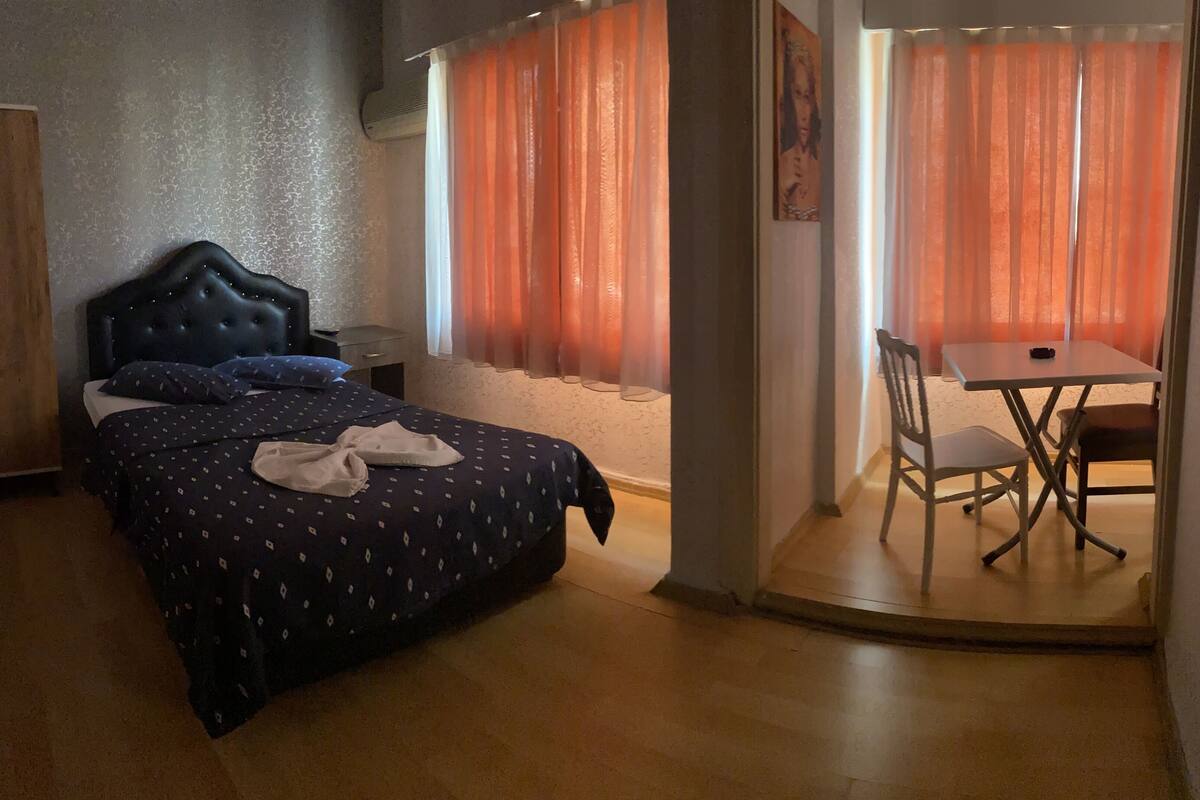 Une chambre à coucher avec un lit, une armoire en bois, une petite table avec une chaise et une fenêtre avec des rideaux orange.