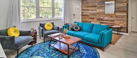 A modern living room with a blue sofa, grey armchairs, a wooden coffee table, and a patterned rug.
