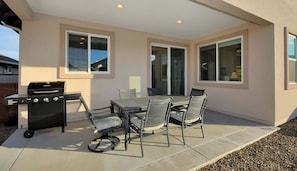 An outdoor patio with a grill, a table, and chairs.