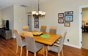 Un comedor con una mesa de madera, seis sillas grises, una lámpara de araña y cuadros en la pared.