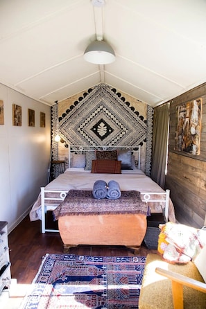A cozy bedroom with a patterned headboard, a bed with rolled towels, a wooden bench, and a rug.