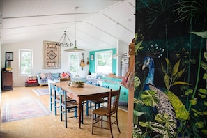 A cozy dining area with a wooden table and chairs, a hanging light fixture, and a colorful wall tapestry.