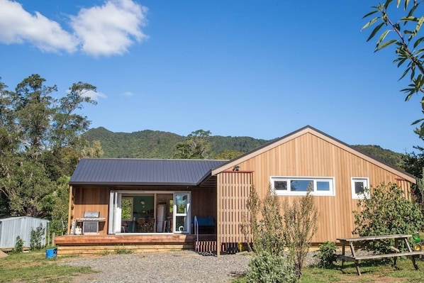 A wooden cabin with a large sliding glass door entrance, a deck, and a small outdoor seating area.
