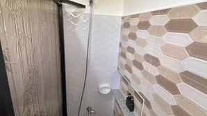 Een badkamer met douche, toilet en een rode emmer.