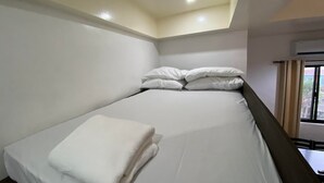 Een eenpersoonsbed met witte lakens, een raam met gordijnen en een airconditioning op de muur.