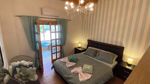 Ein Schlafzimmer mit Bett, Nachttischen, einer Chandelüster, einem Fenster mit Vorhängen und einer Klimaanlage.