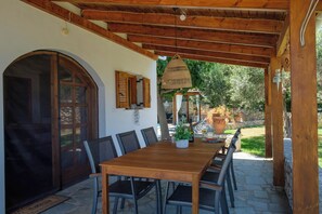 Eine hölzerne Pergola mit Tisch und Stühlen, eine Steinmauer und ein Blick auf einen Garten.