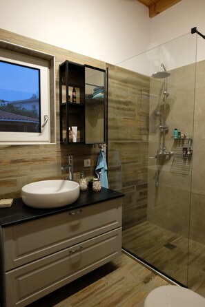 Ein modernes Badezimmer mit einem großen Waschbecken, einer Duschkabine und Holzboden.