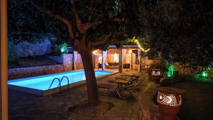 Un espace extérieur avec une piscine, un chemin en pierre, des chaises longues et un mur en pierre.