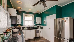 Una cocina moderna con paredes verde azulado, gabinetes blancos, un refrigerador de acero inoxidable y una encimera de granito.