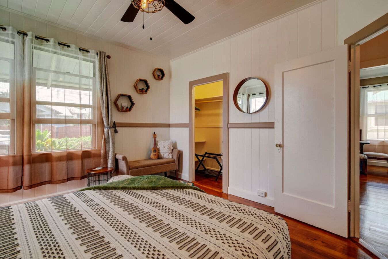 A bedroom with a large bed, a guitar, a chair, a mirror, and a wardrobe.