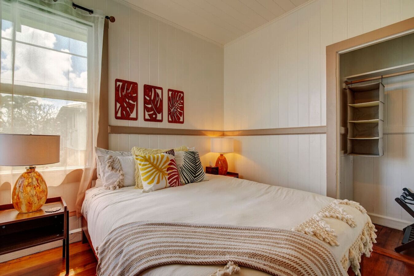 A neatly arranged bedroom with a bed, bedside lamps, a window with curtains, and wall art.