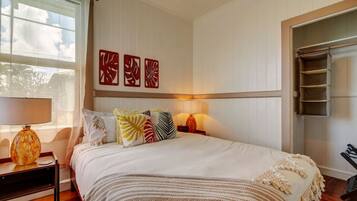 A neatly arranged bedroom with a bed, bedside lamps, a window with curtains, and wall art.