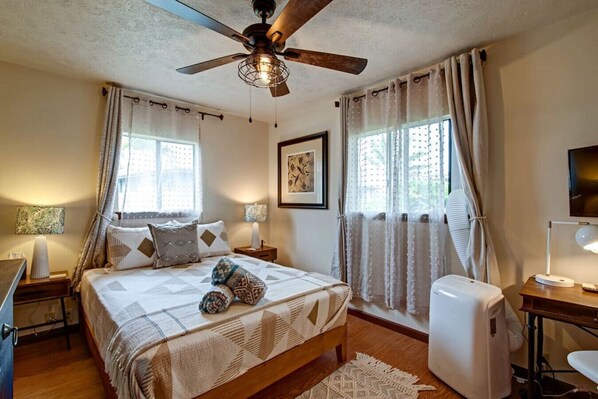 A bedroom with a bed, two bedside tables, a ceiling fan, a TV, and a window with curtains. - NEW - THE OUTRIGGER 3BR 2Bath - Hilo cold AC (Hilo)