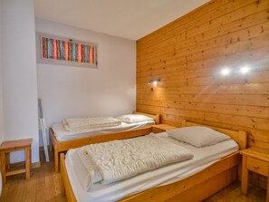 A room with two wooden beds, a small wooden table, and a window with colorful curtains.