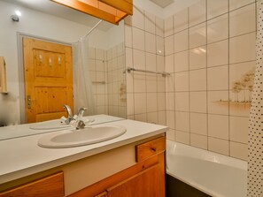 A bathroom with a wooden door, a sink with a mirror, and a bathtub.