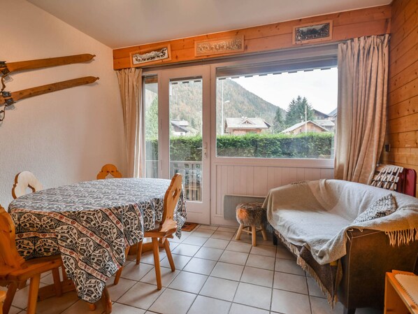 A cozy room with a wooden table and chairs, a sofa, and a window with a view of houses and mountains.