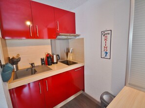 Une cuisine de taille réduite avec des placards rouges, un évier en acier inoxydable et une machine à café.