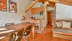 A modern kitchen with wooden cabinets, a central island, and a dining area with a wooden table and chairs. - Cozy 6-Person Apt, Near Center & Pistes, Parking, Balcony, Ski Locker, MultiPass Summer 2024 (Morzine)