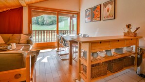 A cozy room with a wooden ceiling, a dining table, chairs, a sofa, and a kitchen area with shelves and a kettle. - Cozy 6-Person Apt, Near Center & Pistes, Parking, Balcony, Ski Locker, MultiPass Summer 2024 (Morzine)
