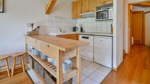 A kitchen with wooden cabinets, a white countertop, a microwave, and a dishwasher. There are stools and baskets under the counter. - Cozy 6-Person Apt, Near Center & Pistes, Parking, Balcony, Ski Locker, MultiPass Summer 2024 (Morzine)