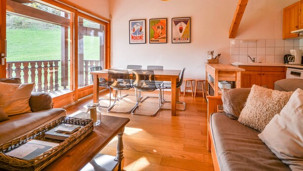 A cozy interior with a wooden dining table, a sofa, and a kitchen area. - Cozy 6-Person Apt, Near Center & Pistes, Parking, Balcony, Ski Locker, MultiPass Summer 2024 (Morzine)