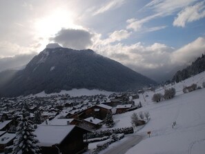 A snow-covered village with traditional wooden houses, a mountain in the background, and a clear sky.