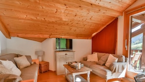 A cozy loft-style living room with a wooden ceiling, a television, a sofa, a coffee table, and a sliding glass door leading to an outdoor area. - Cozy 6-Person Apt, Near Center & Pistes, Parking, Balcony, Ski Locker, MultiPass Summer 2024 (Morzine)