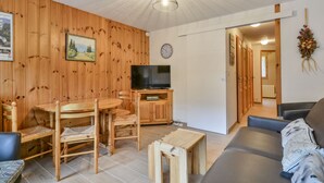 En hyggelig stue med trævægge, et spiseområde med et rundt bord og stole, et fladskærms-tv og en sofa.