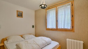 Et soveværelse med en træseng, hvide sengetøj, et vindue med blondegardiner, en radiator og et lille billede på væggen.
