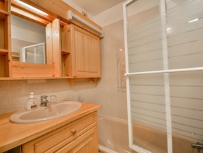 Een badkamer met houten kastjes, een wastafel, een spiegel en een douche met ruitverdelende glazen deuren.