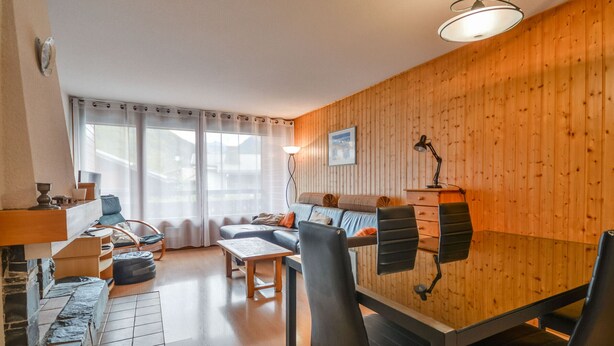Ett mysigt vardagsrum med en väggpanel av trä, en soffa, ett soffbord och en matplats med stolar.