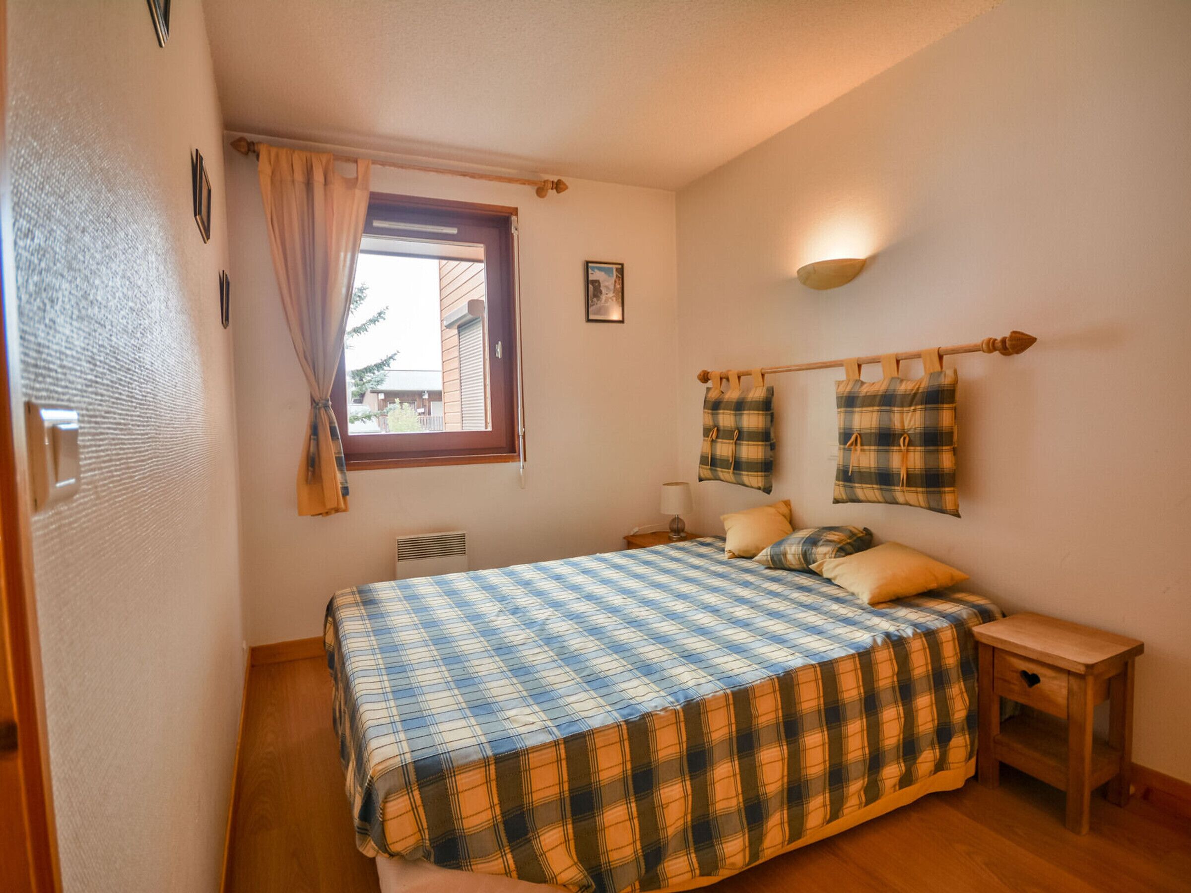 A bedroom with a bed, a window, a bedside table, and a wall-mounted lamp.