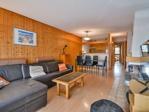A cozy living room with a wooden wall, a sofa, a coffee table, and a dining area with chairs and a table. - Central Morzine Apt, near slopes, sleeps 5, balcony, parking, WiFi, linens included (Morzine)