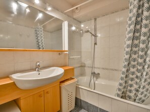 Un baño con un lavamanos blanco, tocador de madera, cabina de ducha de vidrio y cortina de baño estampada.