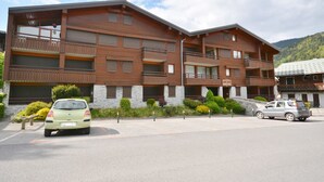 Ett hotell med flera våningar, balkonger, en fasad av sten och en parkeringsplats med bilar.