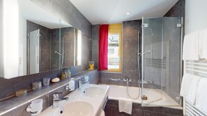 Ein modernes Badezimmer mit einem großen Spiegel, zwei Waschbecken, einer Dusche und einem Duschbereich mit Glastrennwand.