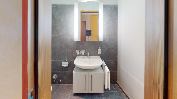 A modern bathroom with a white sink, two towel racks, a mirror, and a toilet visible through an open door.