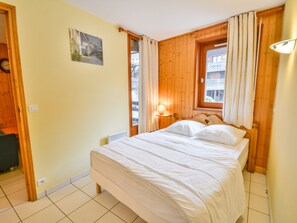A bedroom with a bed, a window with curtains, a bedside lamp, and a wall-mounted clock.