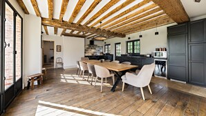 A spacious dining area with a wooden table and chairs, a kitchen with dark cabinets, and a rustic ceiling with exposed beams. - Magnificent house in Normandy (ROSAY SUR LIEURE)