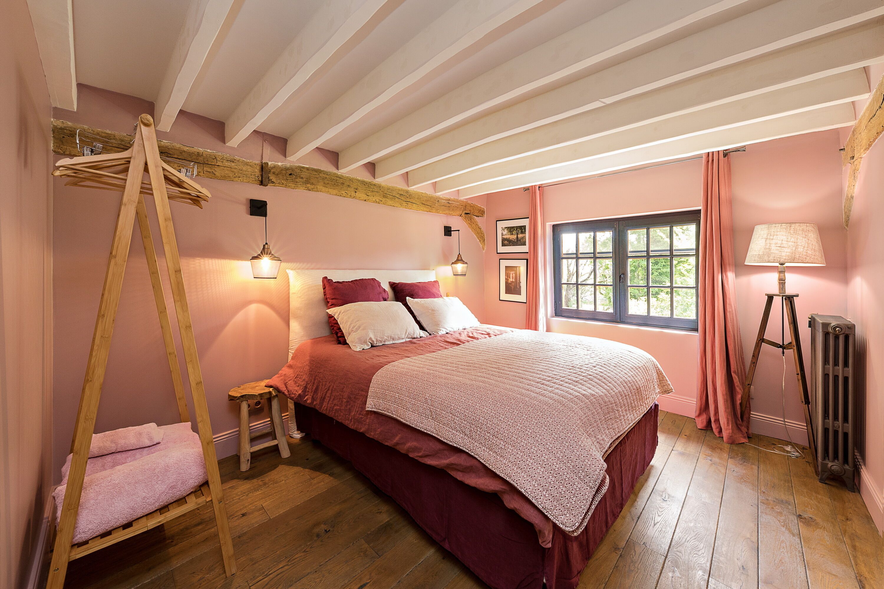 Ein Schlafzimmer mit Bett, Holzboden, einem Hängekorbstuhl, einem kleinen Hocker, einem Fenster mit Vorhängen und einer Heizung.