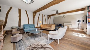 A spacious loft with exposed wooden beams, a cozy seating area with a blue sofa and armchairs, a piano, and a bookshelf. - Magnificent house in Normandy (ROSAY SUR LIEURE)