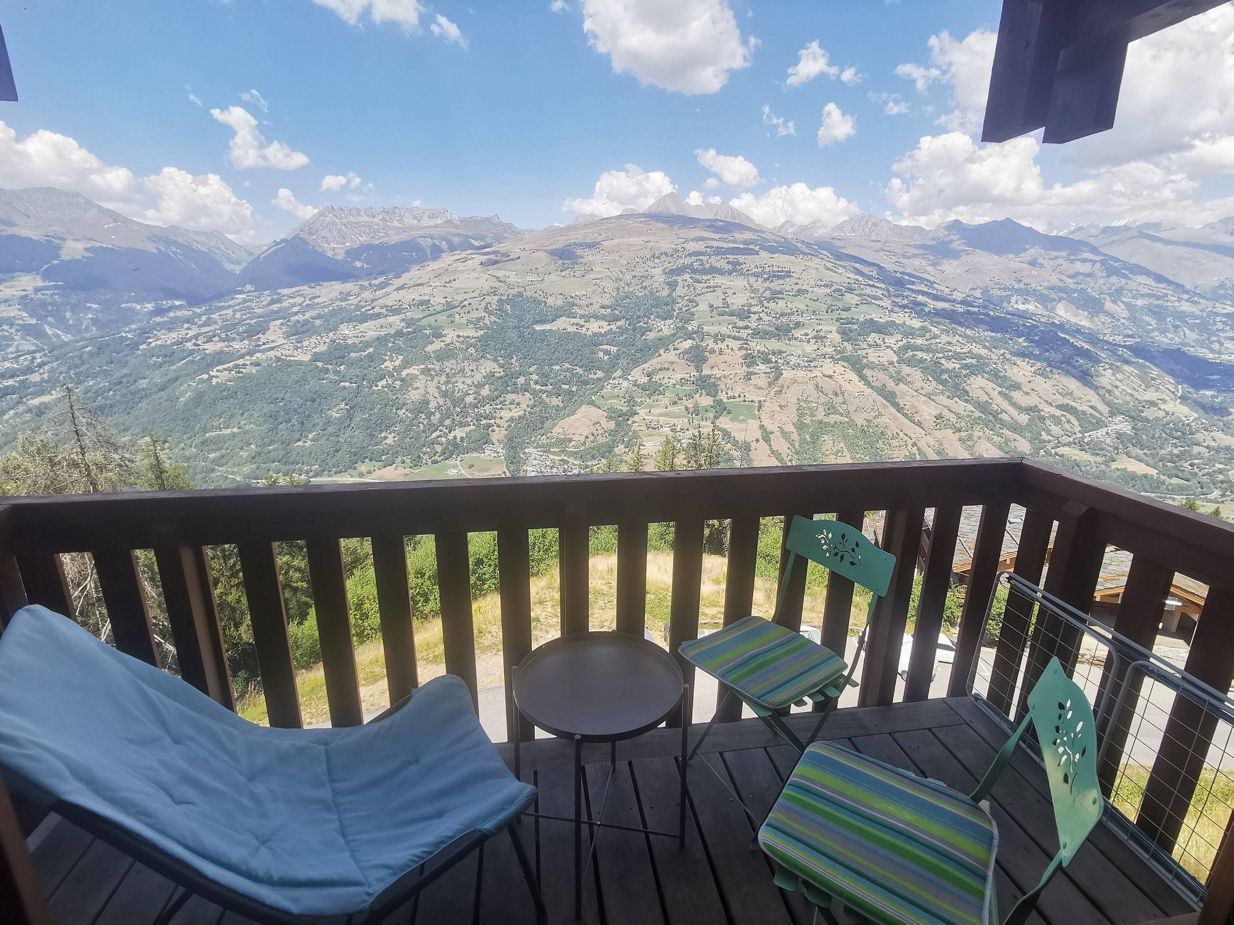 Een terras met twee ligstoelen en een kleine tafel, met uitzicht op een bergachtig landschap.