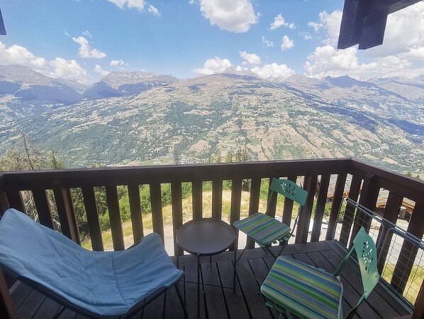 A deck with two lounge chairs and a small table, overlooking a mountainous landscape.