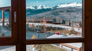 A view through a window of a building with a mountain backdrop, featuring a stone building with a sloped roof and a clear sky. - 3-room apartment with balcony, WIFI, parking and pool access, Les Arcs 1800 (Les Arcs 1800)