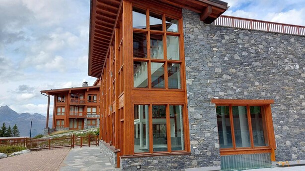 A modern building with a stone facade and large windows, featuring a wooden balcony and a view of mountains. - 3-room apartment with balcony, WIFI, parking and pool access, Les Arcs 1800 (Les Arcs 1800)