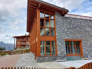 Ein modernes Gebäude mit Natursteinfassade und großen Fenstern, ausgestattet mit einem Holzbalkon und Blick auf Berge.